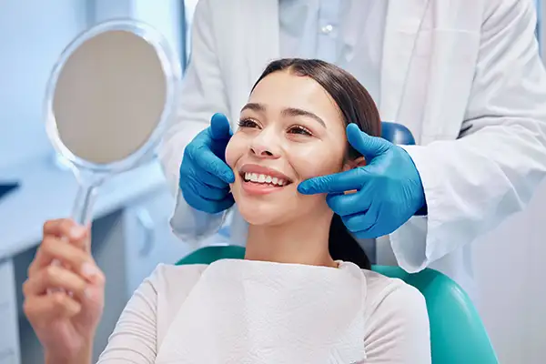 Patient smiling in dental chair while dentist demonstrates teeth after professional cleaning, emphasizing oral health and dental care.