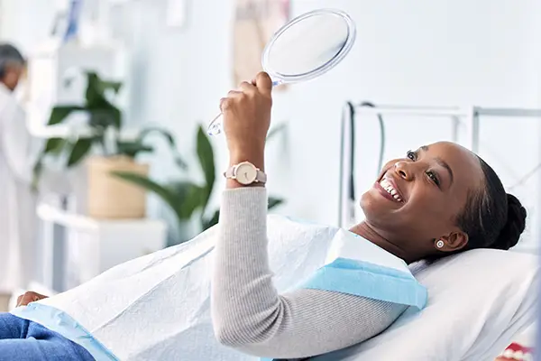 Smiling patient holding a mirror during a dental cleaning appointment at a modern dental clinic, showcasing a positive experience in maintaining oral health.