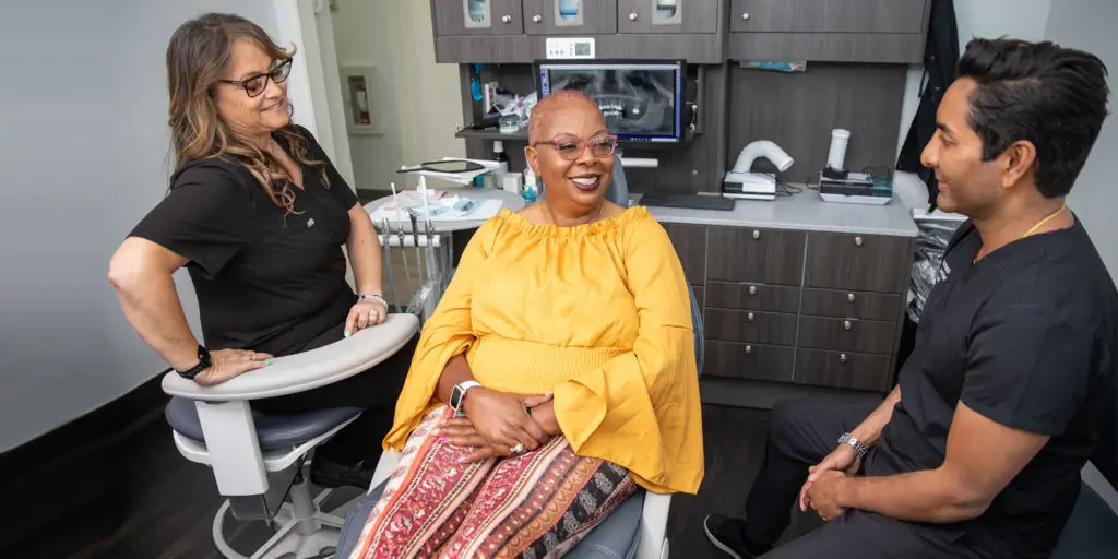 Patient smiling in a dental chair, conversing with two dental professionals in a modern clinic, emphasizing a comfortable and supportive environment for oral surgery and sedation dentistry.