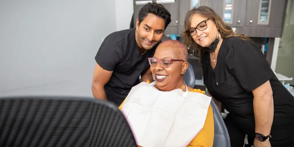 Smiling patient with short hair in dental chair, surrounded by two dental professionals, showcasing a positive dental experience at Palani Center for Dental Implants.