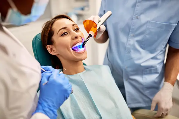 Patient receiving dental bonding treatment at Palani Center for Dental Implants, with dental professionals using a curing light to enhance smile aesthetics.