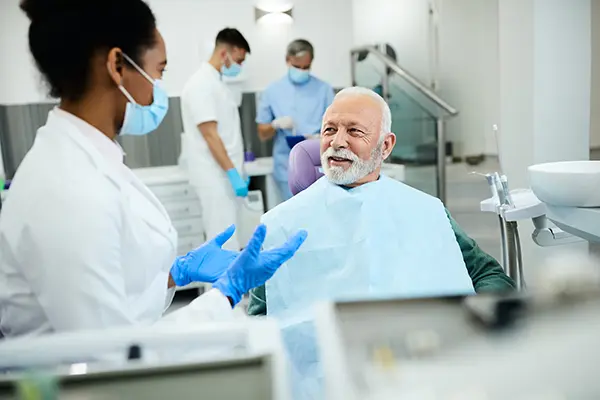 Dental exam at Palani Center for Dental Implants, patient in dental chair smiling, dentist discussing oral health, staff in background, modern clinic setting.